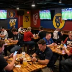 Penggemar yang terlibat menikmati Taruhan Bola di bar olahraga, memasang taruhan di smartphone mereka